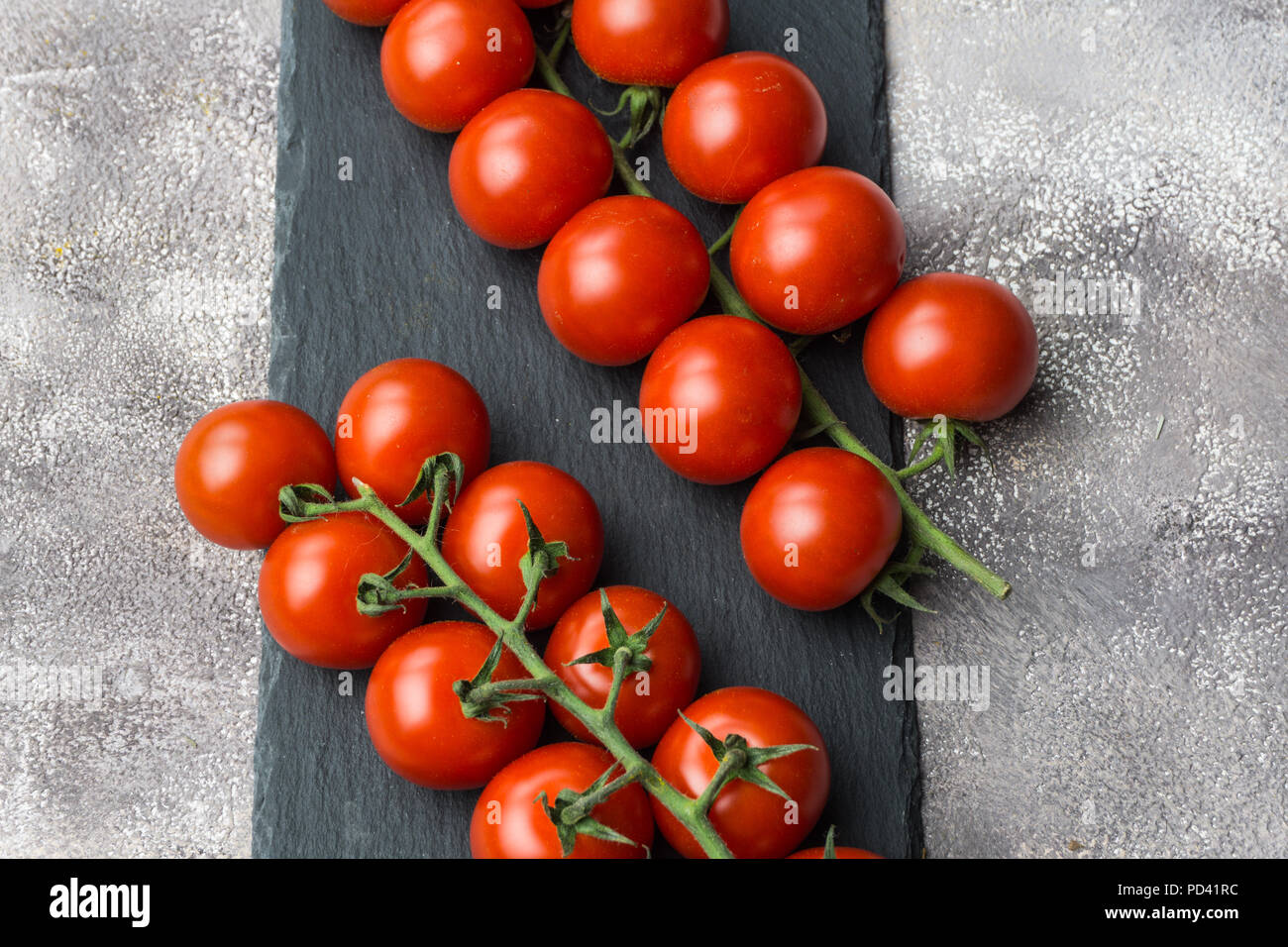 Frische Kirschtomaten auf einem Zweig auf einem schwarzen konkreten Hintergrund. Stockfoto