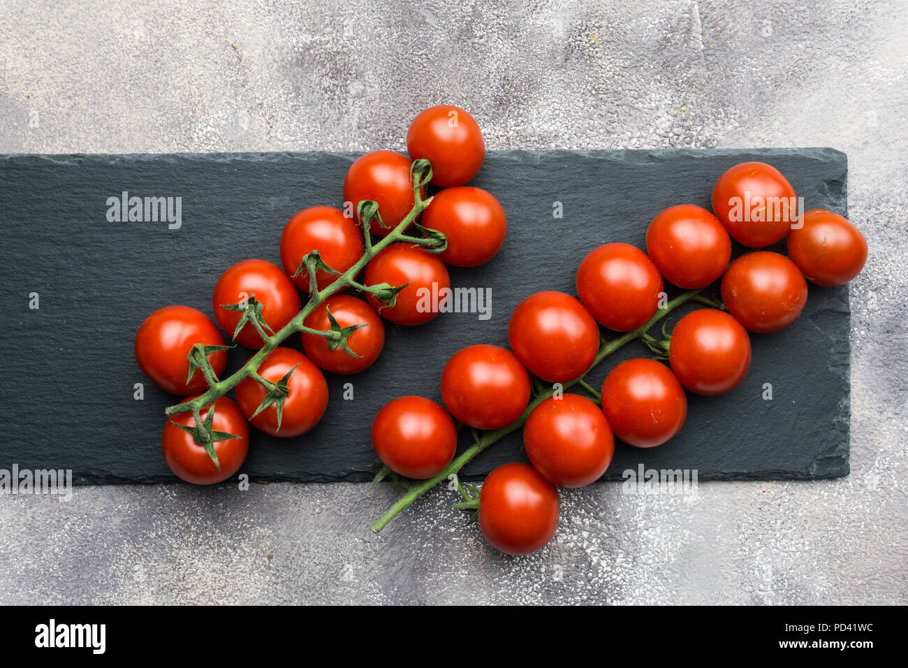 Frische Kirschtomaten auf einem Zweig auf einem schwarzen konkreten Hintergrund. Stockfoto