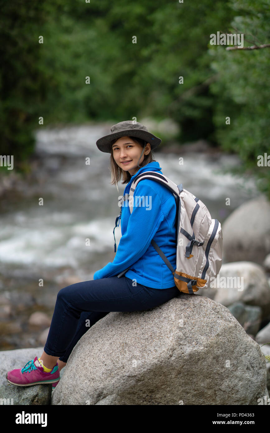 Lächelnd Wanderer Mädchen mit weißen Rucksack auf einem Stein saß Stockfoto