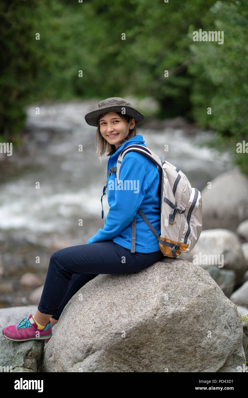 Lächelnd Wanderer Mädchen mit weißen Rucksack auf einem Stein saß Stockfoto