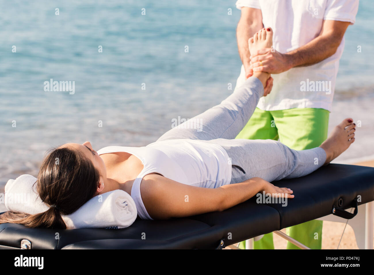 Der junge Athlet mit knöchelverletzung in Kurativen osteopathische Behandlung im Freien. Mädchen mit auf Massage mit Therapeuten im Hintergrund Mann beg Stockfoto
