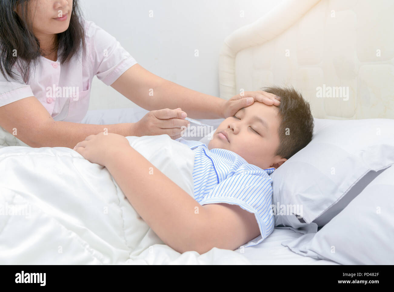Mutter Temperaturmessung von ihr krankes Kind. Kranker Junge mit Thermometer Festlegung auf dem Bett und Mutter Hand, denn Temperatur. Krankes Kind mit Fieber und Kranke Stockfoto