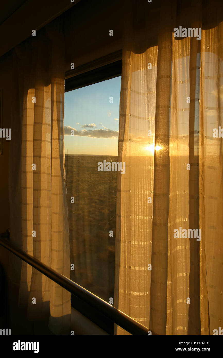 Orange Sonnenuntergang durch das Fenster und Vorhang auf dem Zug Stockfoto