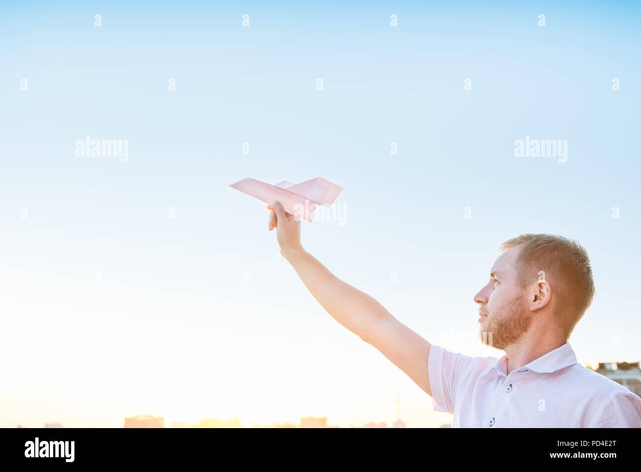 Der Mann hält Papierflieger in blauer Himmel bei Sonnenuntergang Licht mit Stadt Landschaft Hintergrund. Träume und Freiheit Konzept. Selektive konzentrieren. Copyspace Stockfoto