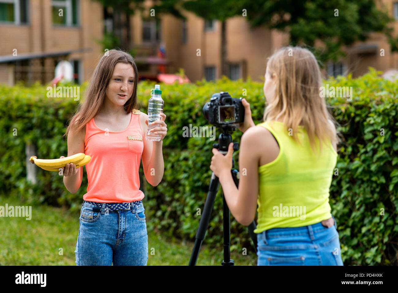 Zwei Mädchen Freundinnen, im Sommer in der Stadt. Video auf der Kamera aufgezeichnet werden. In den Händen halten sie eine Banane Flasche Wasser. Das Konzept der gesunden Ernährung. Verwenden Sie die Kamera mit einem Stativ. Stockfoto
