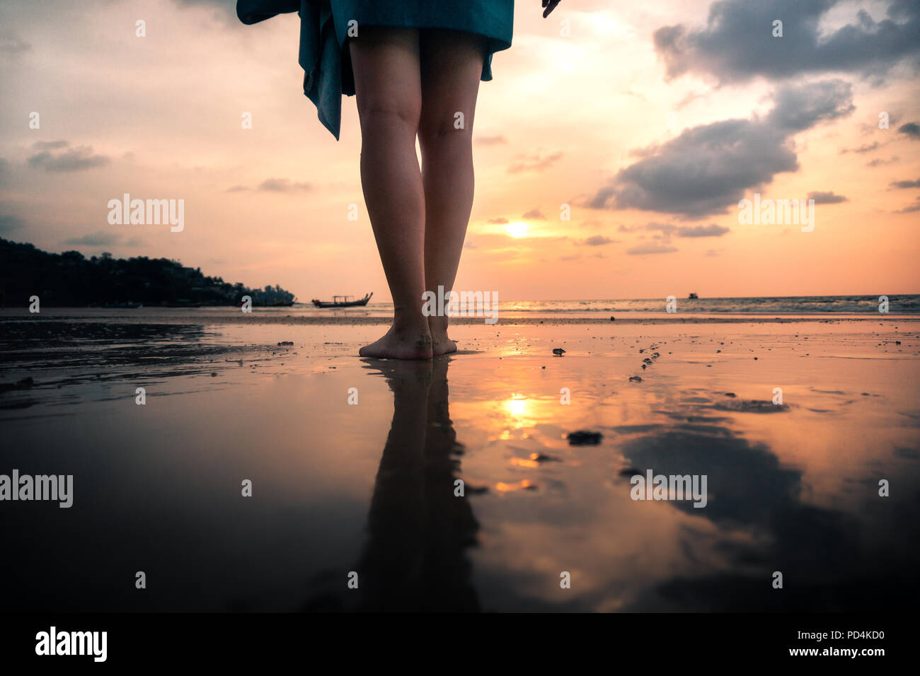Beine der jungen Frau von hinten stehend auf Strand vor Golden Sunset im Urlaub Stockfoto