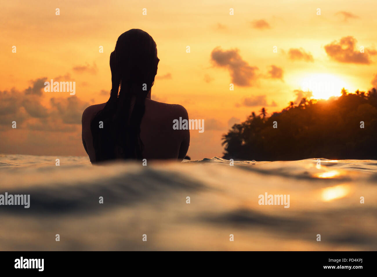 Junge Frau von hinten im Indischen Ozean während orange Sonnenuntergang mit romantischer Stimmung Stockfoto