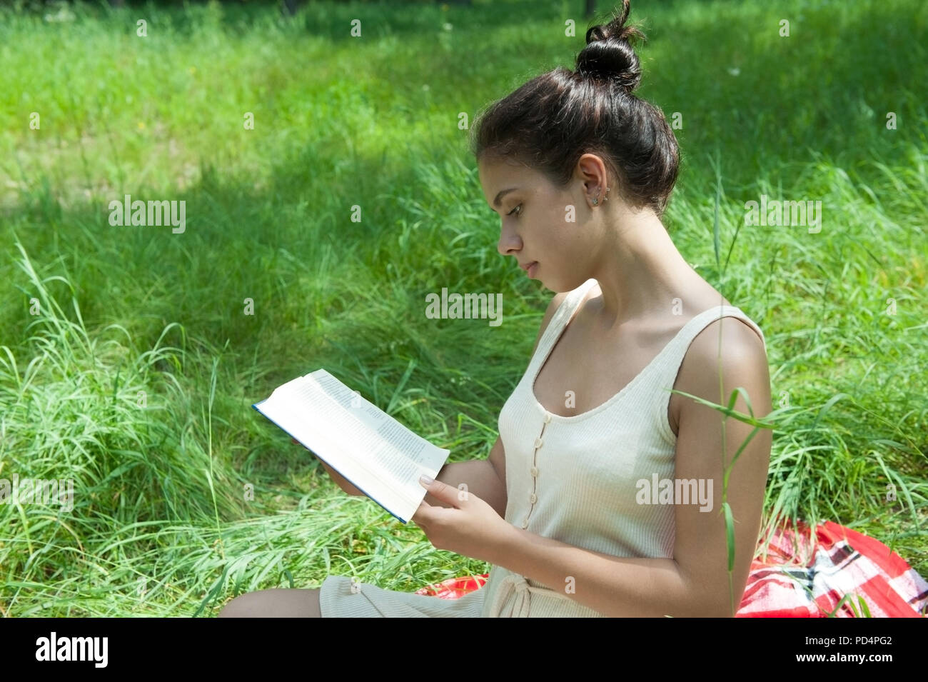 Ein Mädchen sitzt auf dem Gras und liest ein Buch Stockfoto