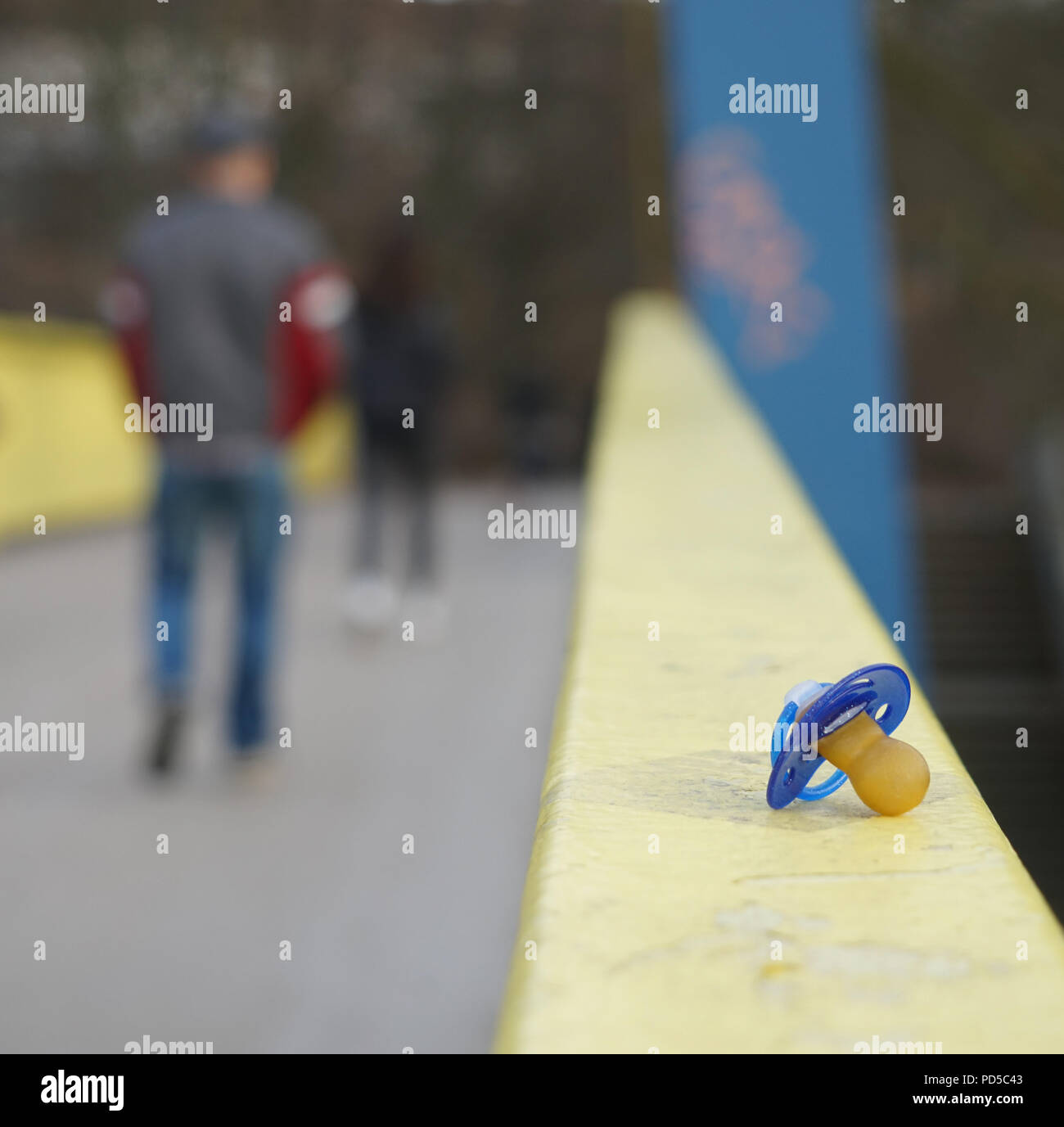 Verlorener Baby-Schnuller auf geländer Geländer, verschwommene Fußgänger, die weggehen, alltäglicher urbaner Moment Stockfoto