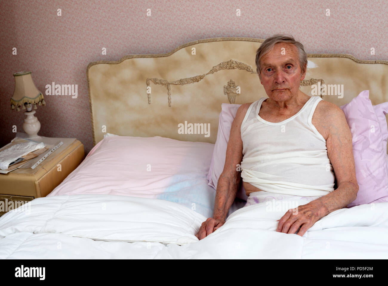 Älterer Mann im Bett sitzend Stockfoto