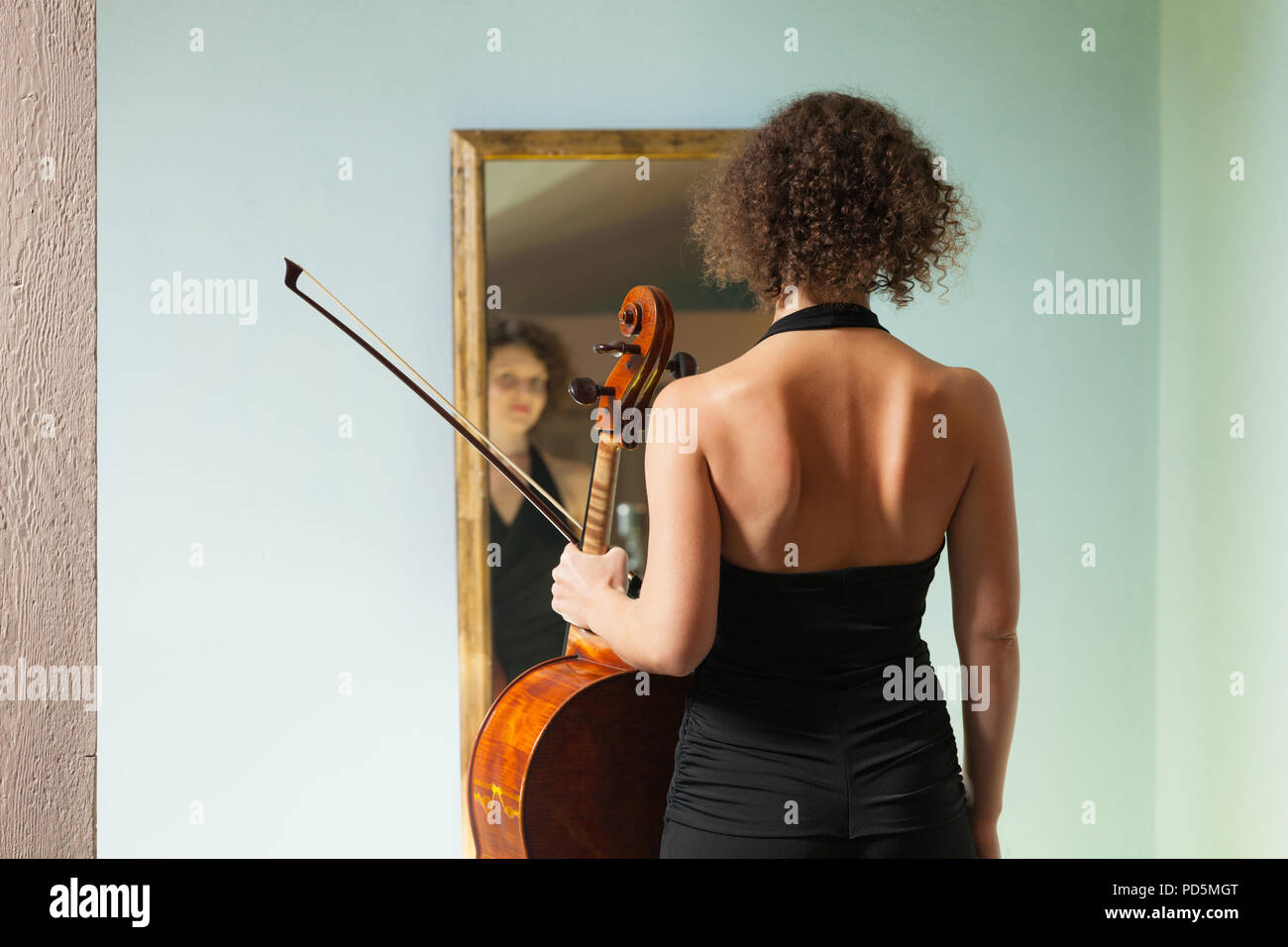 Schöne Frau mit Cello, in einem Spiegel sich selbst Stockfoto