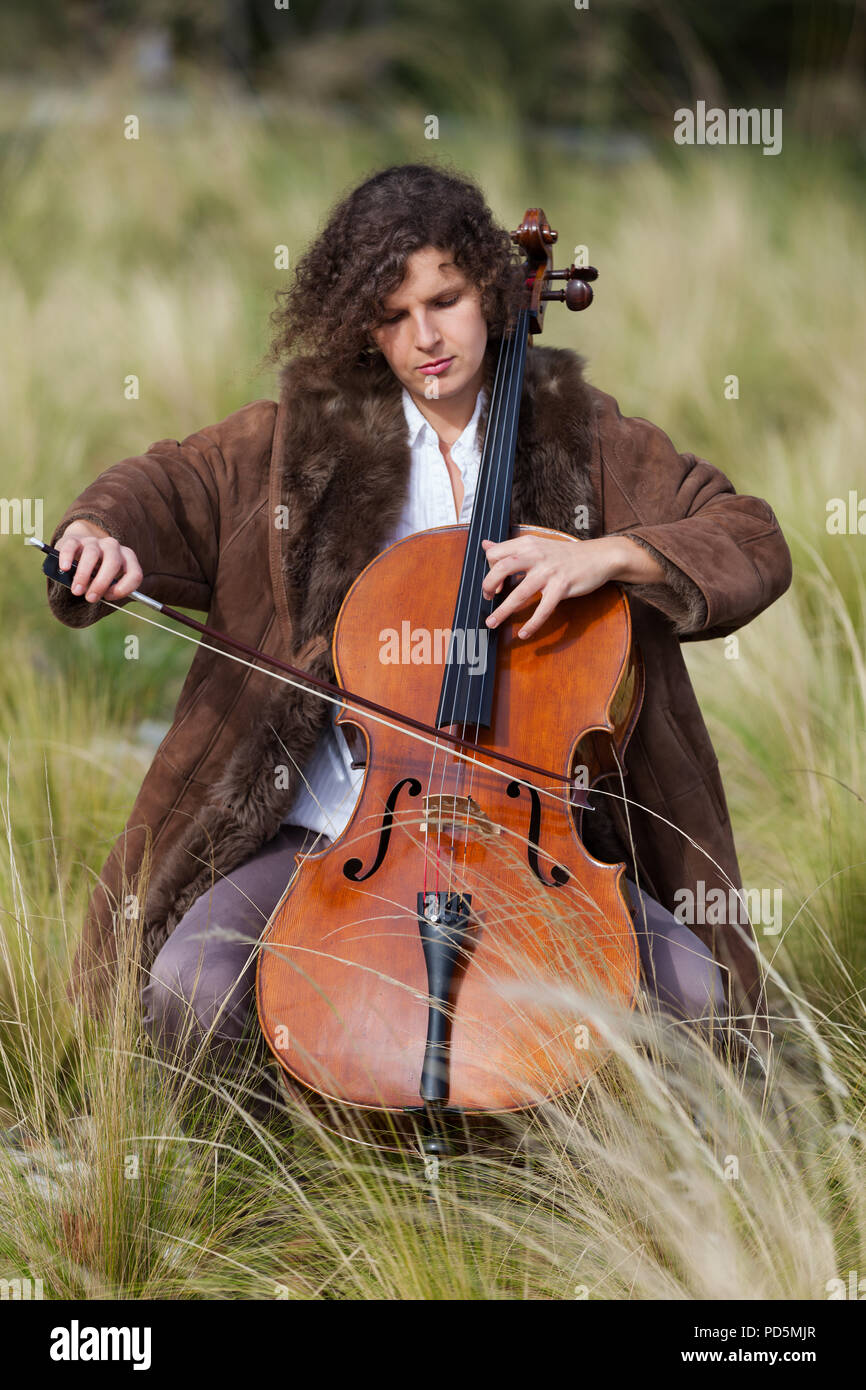 Frau spielt das Cello zwischen Feldern Stockfoto