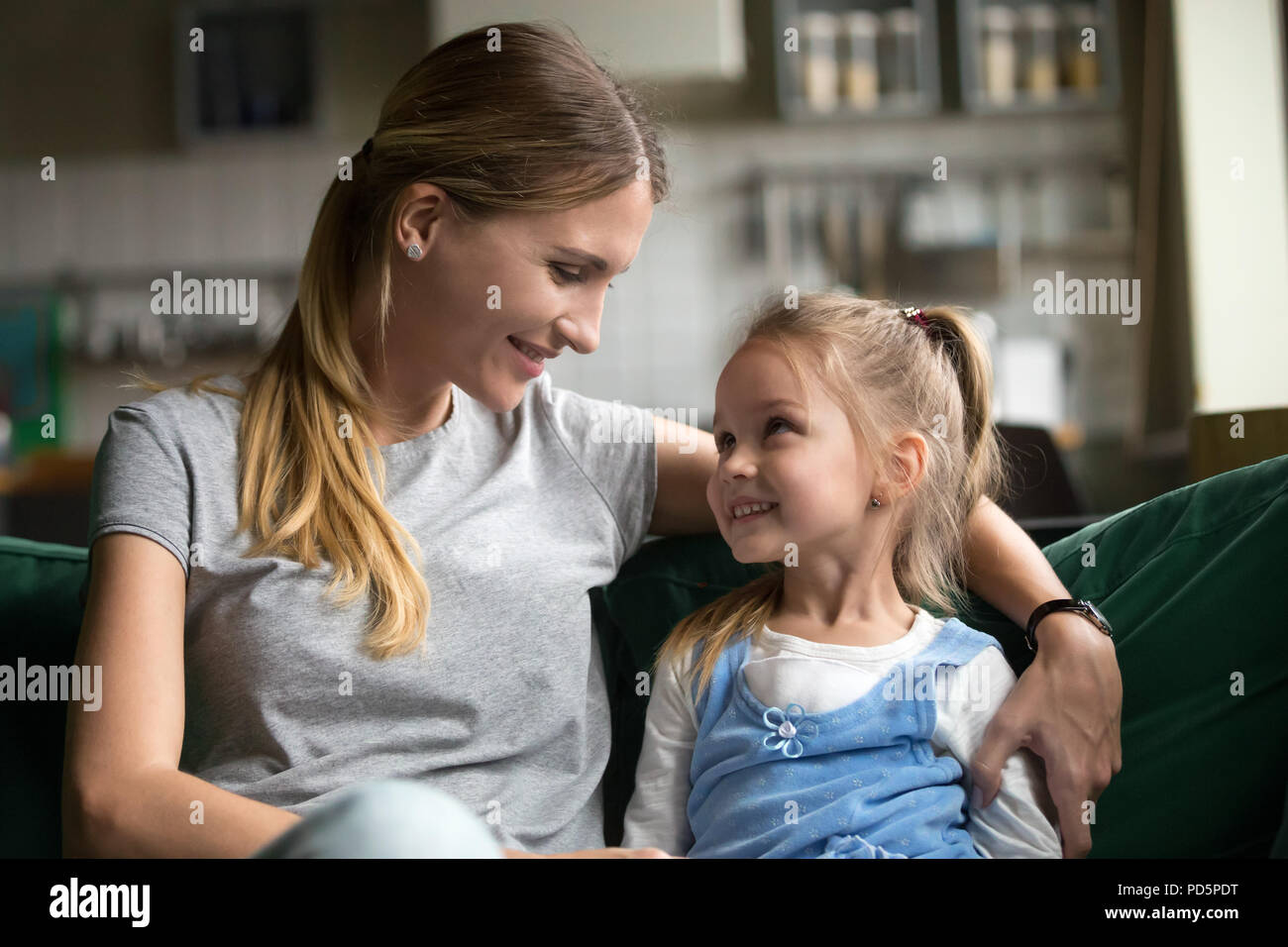 Lächelnd Kind Tochter an liebevolle Mutter umarmt auf dem Sofa auf der Suche Stockfoto