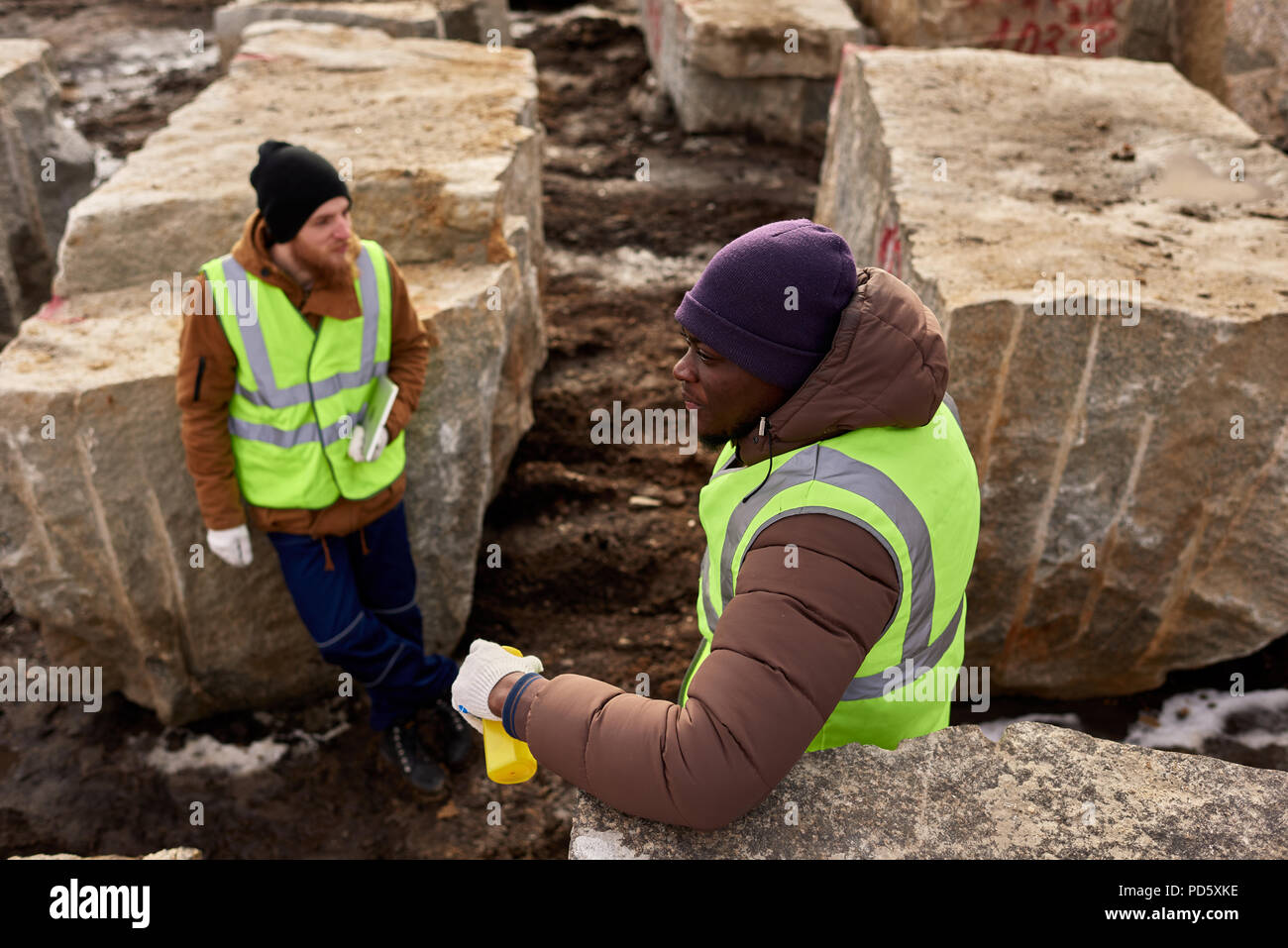 Hohe Betrachtungswinkel von zwei industriellen Arbeitskräfte, die reflektierende Jacken ruht sich gegen Granit über den Bergbau Baustelle im Freien Stockfoto