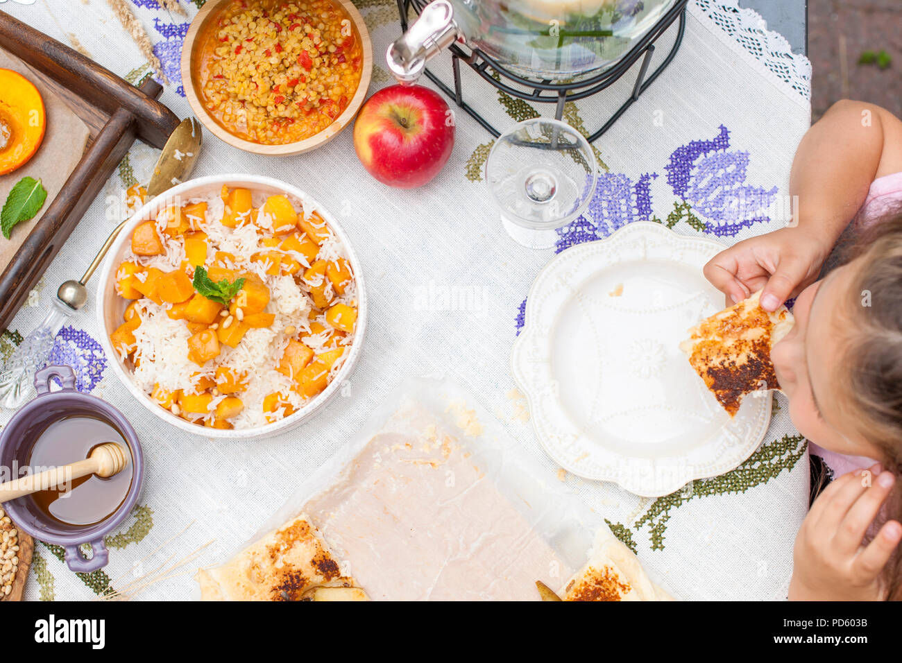 Kleines Mädchen isst Kuchen. Familienessen im Innenhof im Freien. Herbstgemüse und Obst auf dem Tisch. Blick von oben auf den Esstisch. Ein besonderer Ort für Text Stockfoto