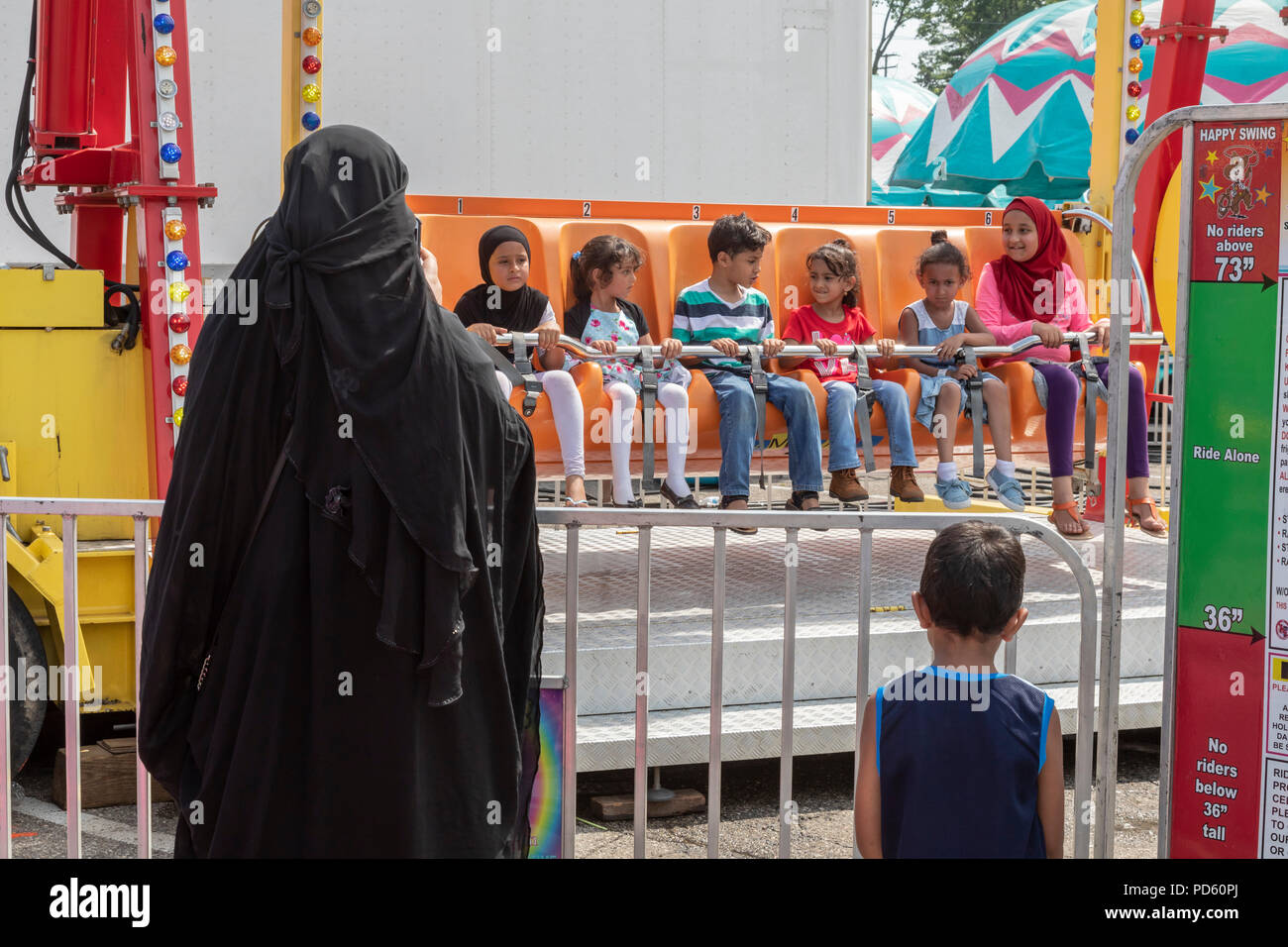Dearborn, Michigan - eine Frau in islamischen Kleidung Uhren Kinder auf der Happy Swing carnival Ride an der jährlichen Dearborn Homecoming Festival. Fast Stockfoto