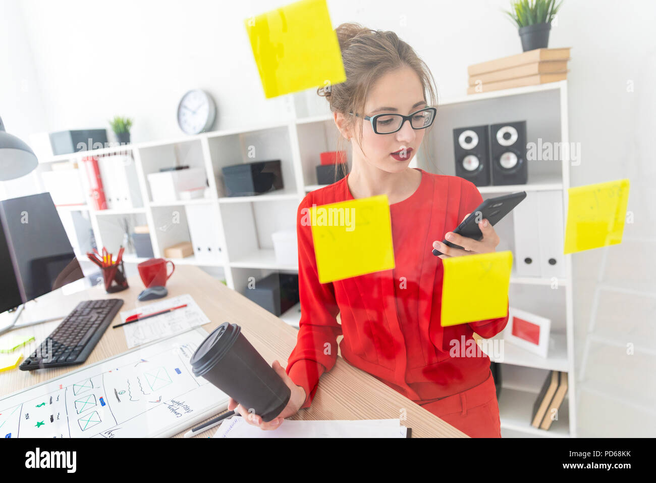 Ein junges Mädchen steht in der Nähe eine transparente Board mit Aufklebern und hält ein Glas mit Kaffee und Telefon. Stockfoto