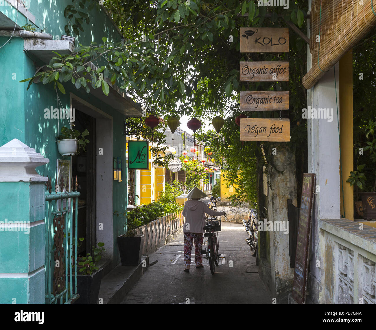 Eine asiatische Dame ist zu Fuß ihr Fahrrad über die Gasse der alten Stadt Hoi An. Stockfoto