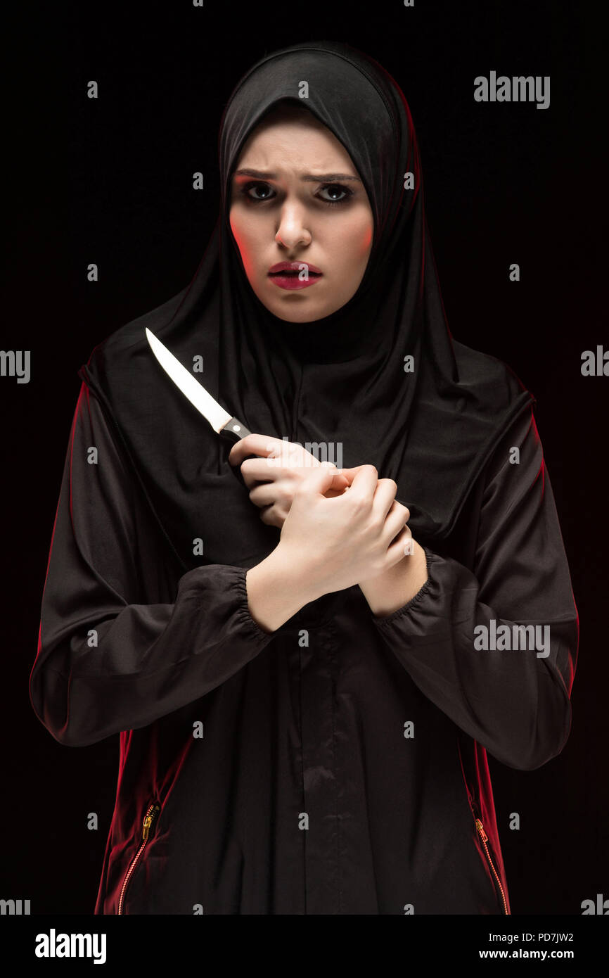 Porträt der Schönen verzweifelte Angst junge muslimische Frau mit schwarzen Hijab holding Messer in ihren Händen als Schutz Konzept auf schwarzem Hintergrund Angst Stockfoto