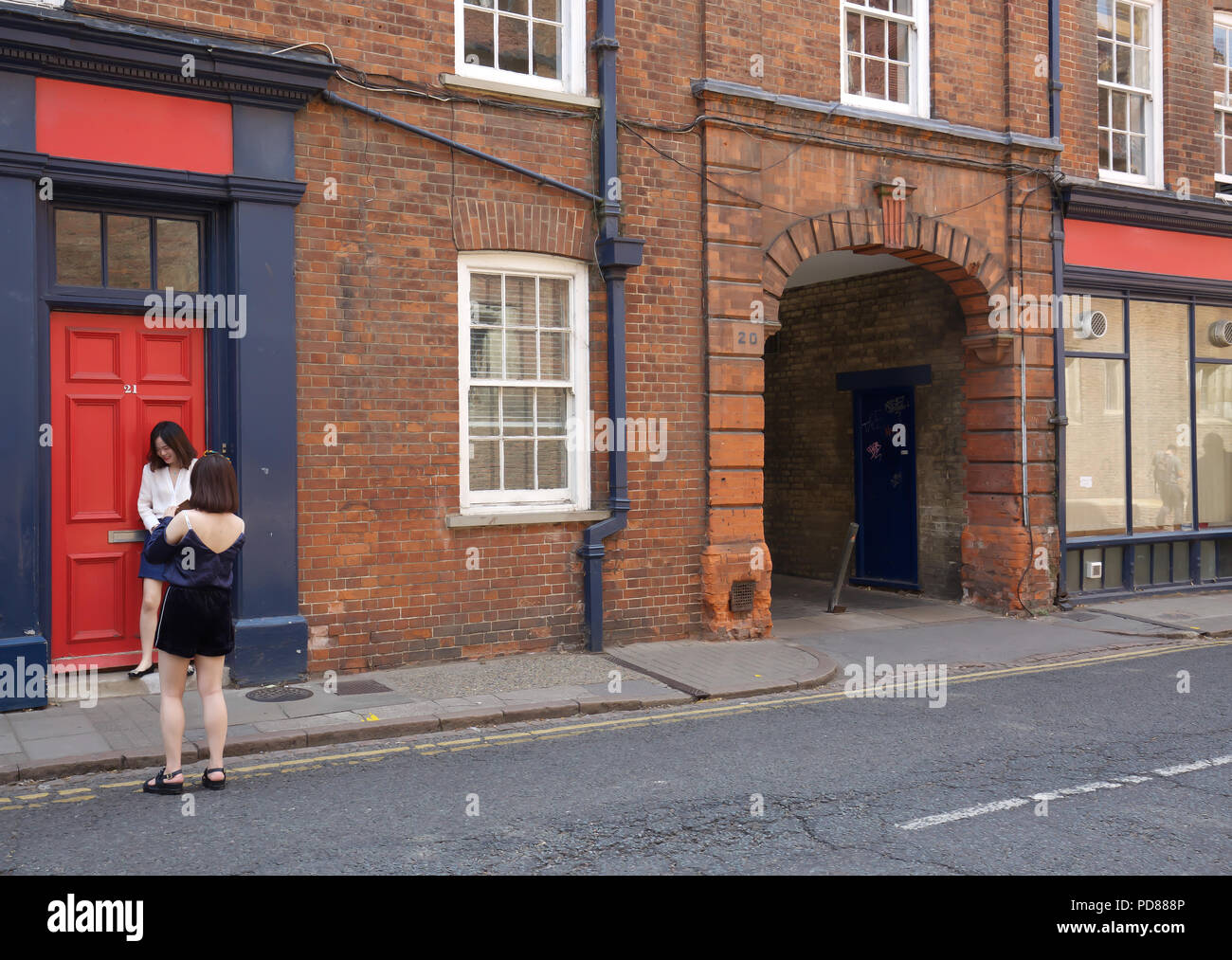 Cambridge, UK, 7. August 2018, eine asiatische Dame stellt durch eine rote Tür in Cambridge, während andere um die historische Stadt und Hochschulen suchen. Das Wetter ist durch Abkühlen nach Gewitter am Abend. Credit Keith Larby/Alamy leben Nachrichten Stockfoto