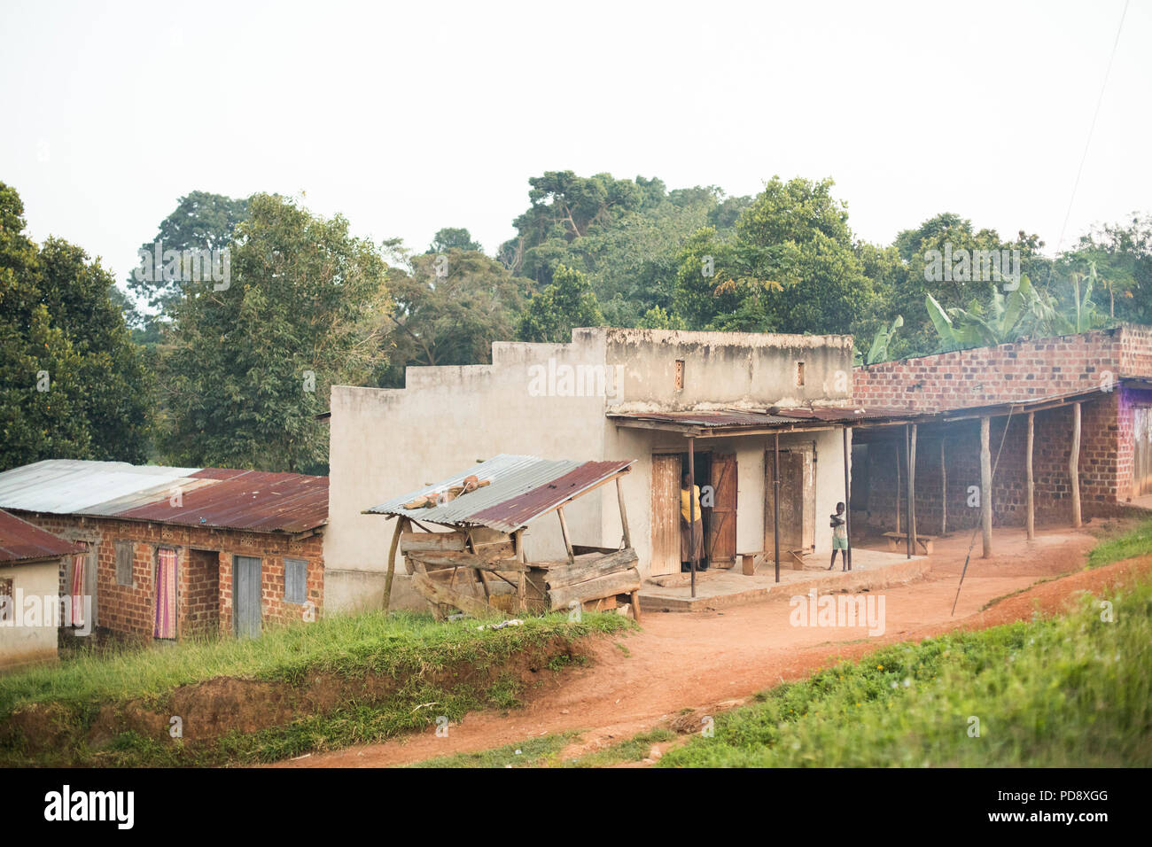 Geschäfte und Häuser säumen den Straßenrand von einer kleinen Stadt im ländlichen Bezirk Mukono, Uganda. Stockfoto