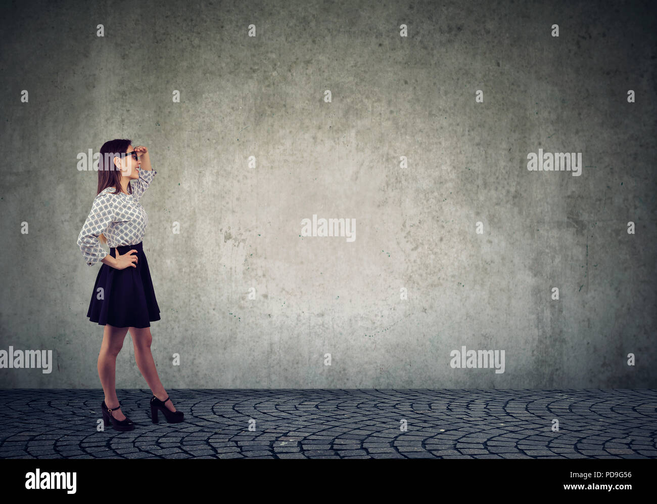 Seitenansicht des jungen trendigen Frau in Gläsern stehen auf grauen Hintergrund und weg auf der Suche nach zukünftigen Pläne Stockfoto
