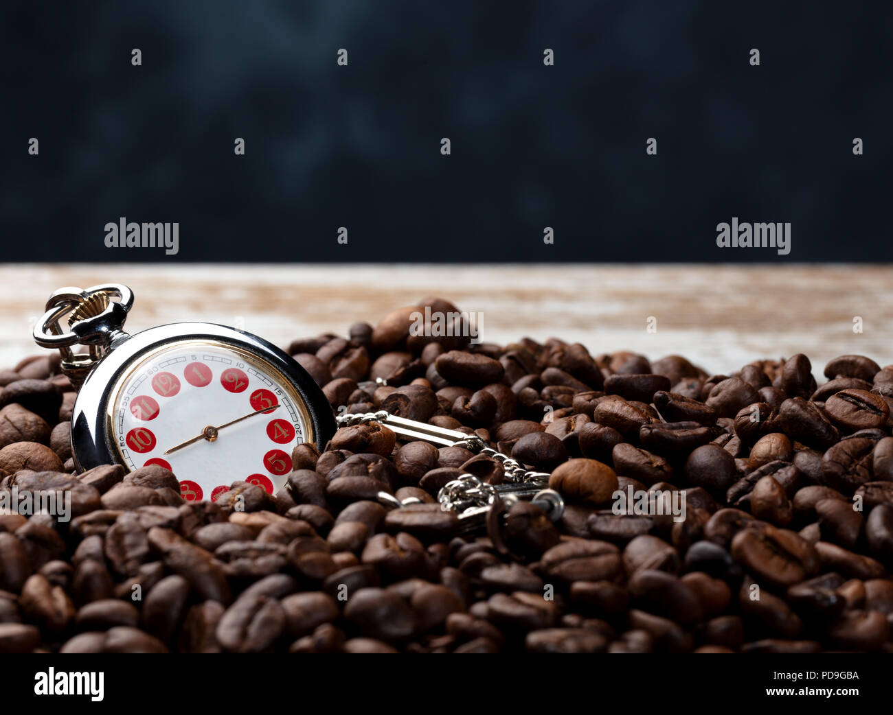 Eine Menge Kaffee Bohnen mit einer Hand auf einem abgenutzten braune Holztisch und blauen Hintergrund, coceptual Foto zeigt, dass es Zeit für einen guten Kaffee Stockfoto