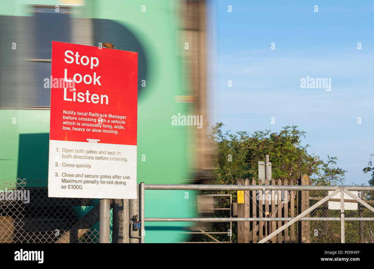 Unbeaufsichtigte Fußgängerzone Bahn Kreuzung mit Stop, Look, Warnschild und eine südliche Zug beschleunigt Vergangenheit in West Sussex, England, UK hören. Stockfoto