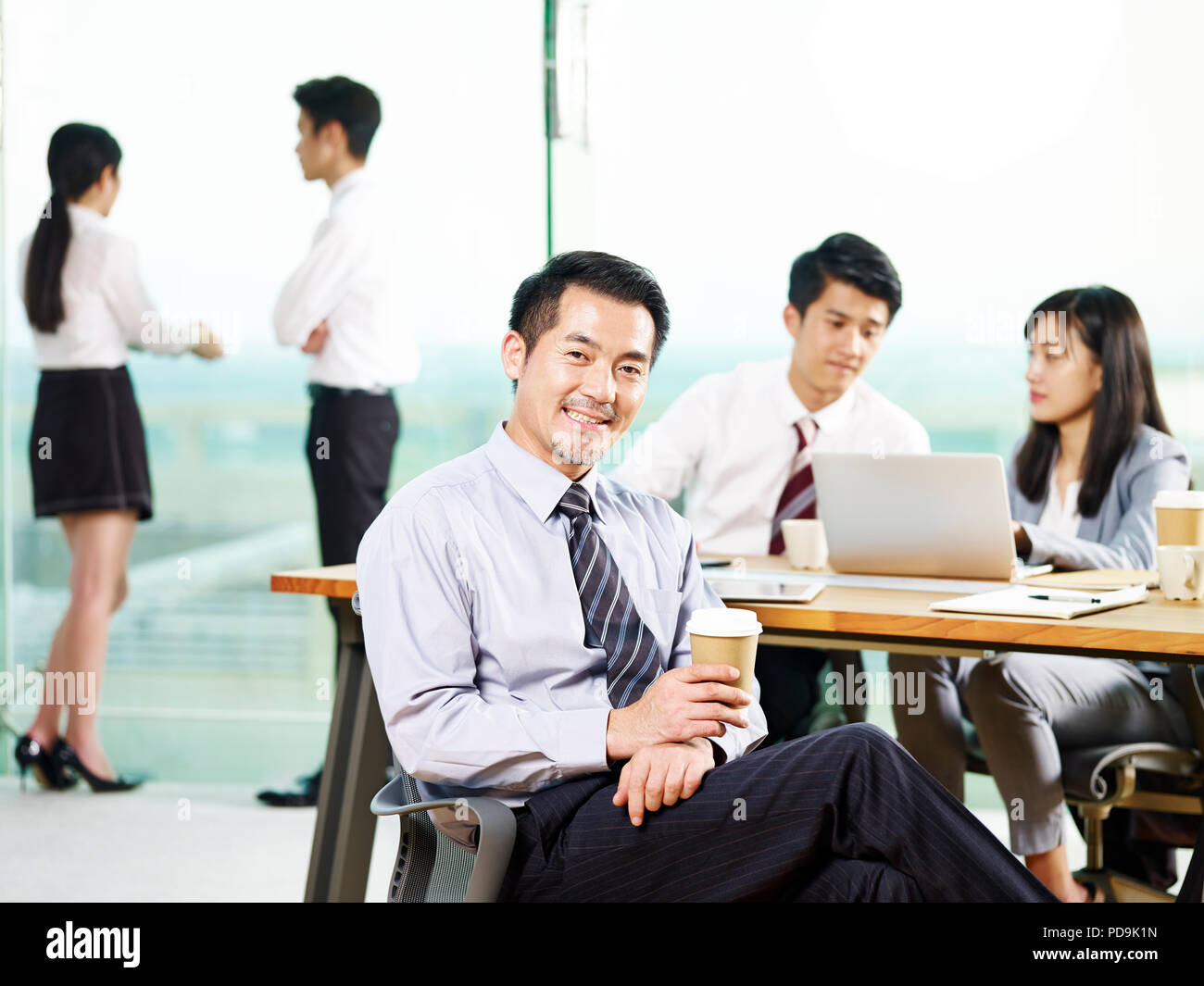 Porträt eines erfolgreichen asiatischen Senior Corporate Manager mit einer Tasse Kaffee in die Kamera lächelnd im Büro suchen. Stockfoto