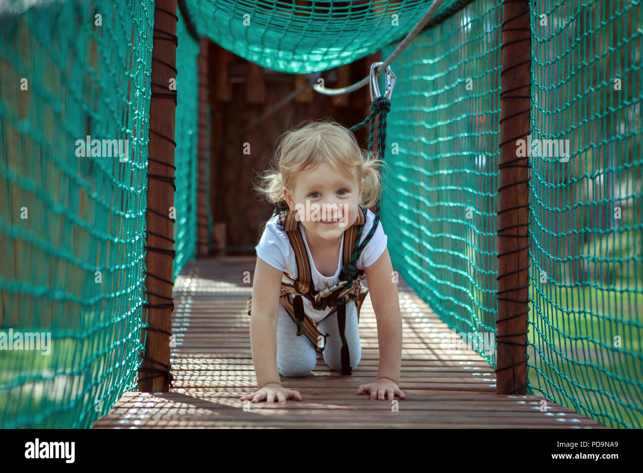 Kleine blonde Mädchen überwindet ein Hindernis im Seilpark. Sie kriechen Stockfoto