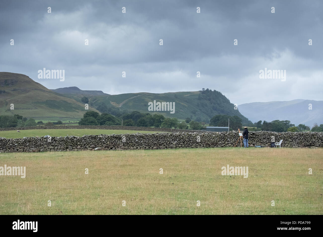 Maler sein Kunstwerk in einem Feld neben Castlerigg Steinkreis und Blick auf den Lake District Berge von helvellyn vor der Mauer aus Stein Stockfoto
