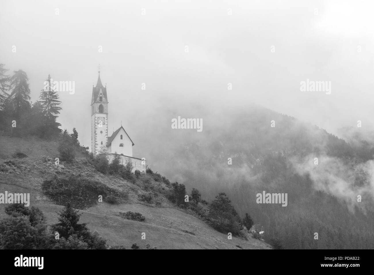 Kirche in Schwarz und Weiß im Nebel auf einem Hügel in die Dolomiten in La Valle, Südtirol, Italien Stockfoto