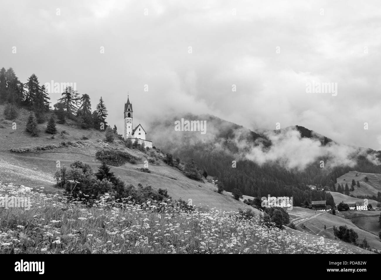 Kirche in Schwarz und Weiß an einem nebligen Hang in die Dolomiten in La Valle, Südtirol, Italien Stockfoto