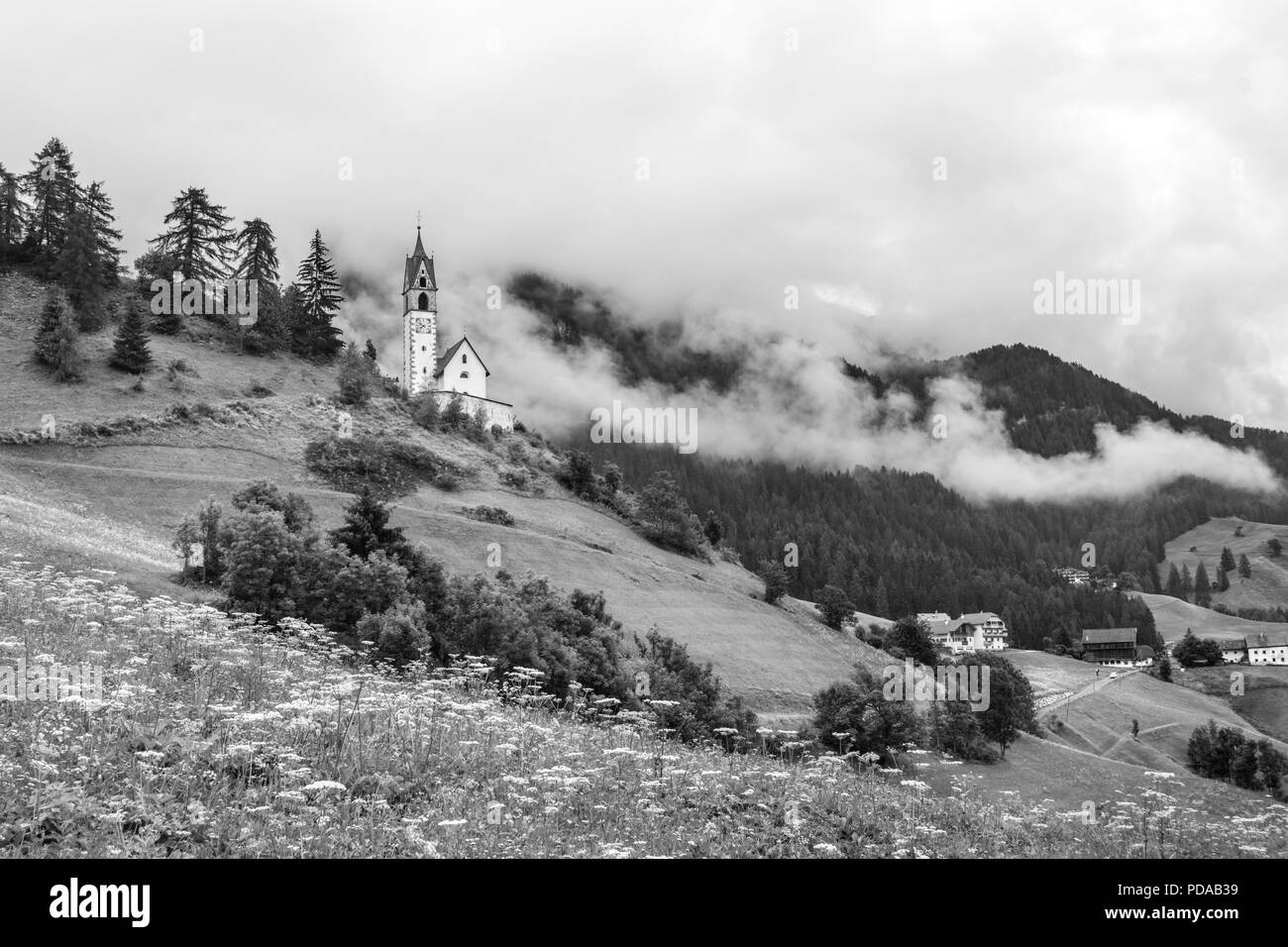 Kirche in Schwarz und Weiß an einem nebligen Hang in die Dolomiten in La Valle, Südtirol, Italien Stockfoto