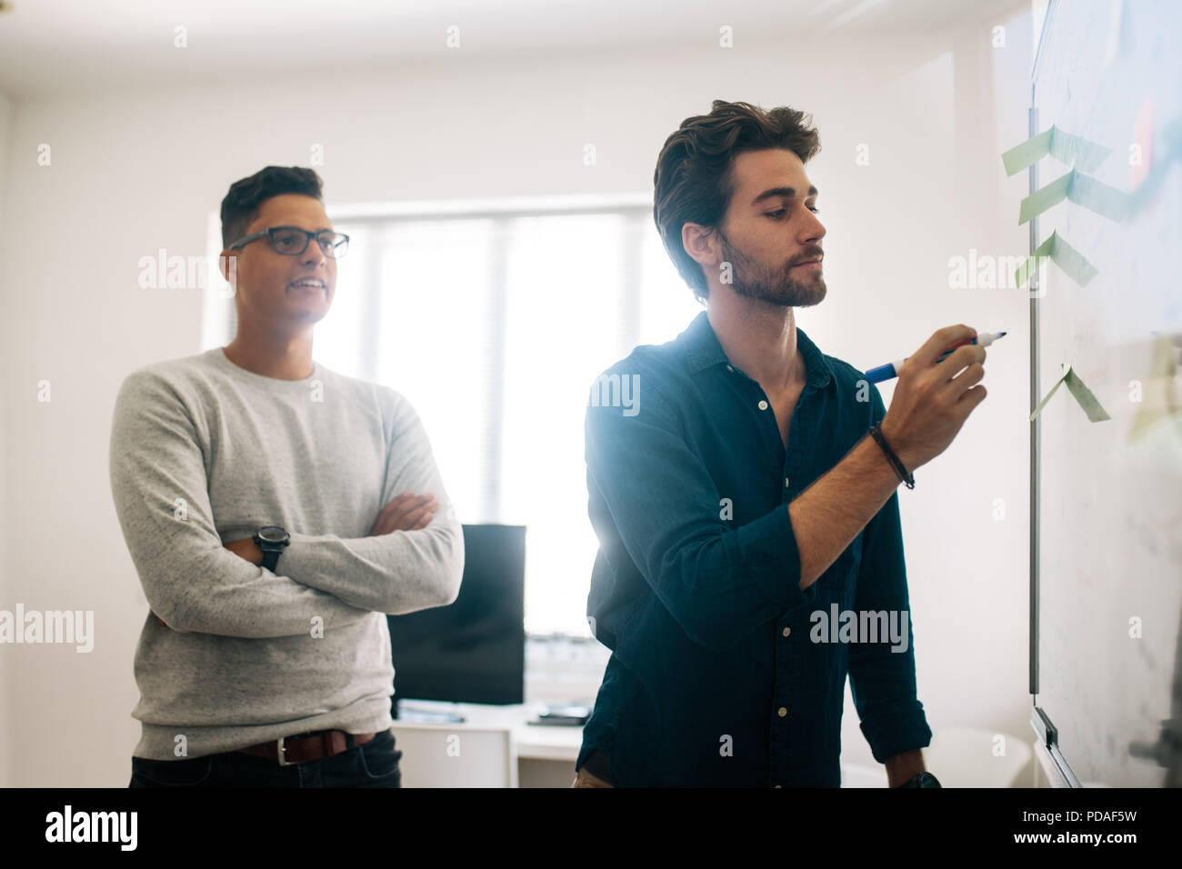 Mann schreiben an Bord im Tagungsraum, während seine Kollegen aussieht. Anwendungsentwickler im Diskutieren von Ideen und Schreiben an Bord Stockfoto
