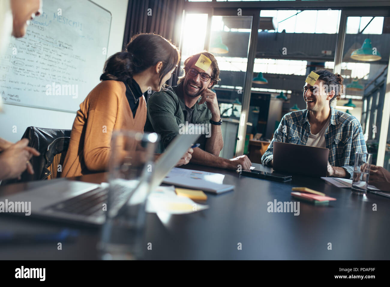 Business Team um einen Tisch im Büro Lobby mit Haftnotizen auf ihre Stirn mit einem Brainstorming Sitzung. Corporate Business Leute sitzen Stockfoto