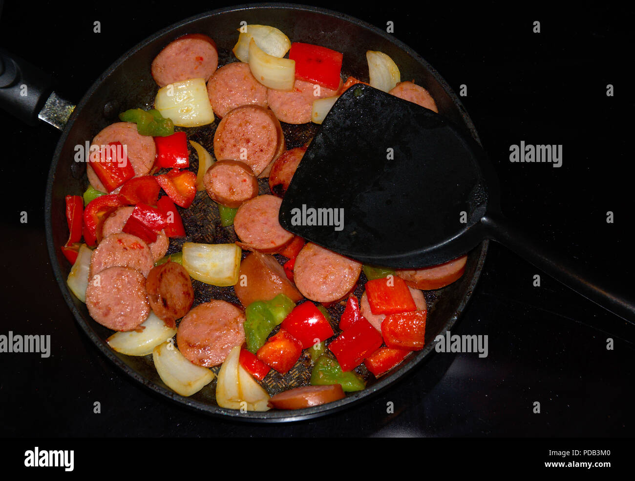 Rühren braten Essen im Topf auf dem Herd mit grünem, rotem Paprika,  Zwiebeln und geräucherte Wurst Stockfotografie - Alamy