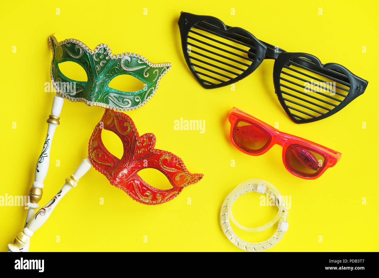 Karneval venezianische Masken in Grün und Rot mit Griff, fancy Gläser und Glitter Armbänder für Photo Booth auf lebendige gelb Hintergrund isoliert, ausgefallenen Stockfoto
