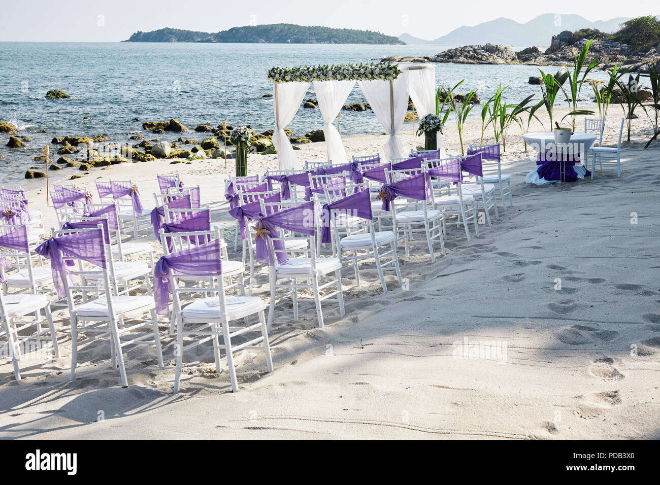 Hochzeit am Strand Veranstaltungsort Einstellungen auf dem weißen Sand am  Meer mit weißen Chiavari Stühle verzieren mit violett organza Schärpe,  minimale Blumenmotiv, p Stockfotografie - Alamy