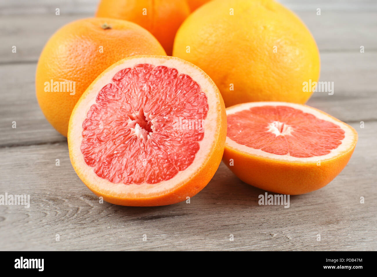 Rosa grapefruit Schnitt zu Hälfte auf Holz Schreibtisch, mit ganzen Zitrusgewächse im Hintergrund. Stockfoto