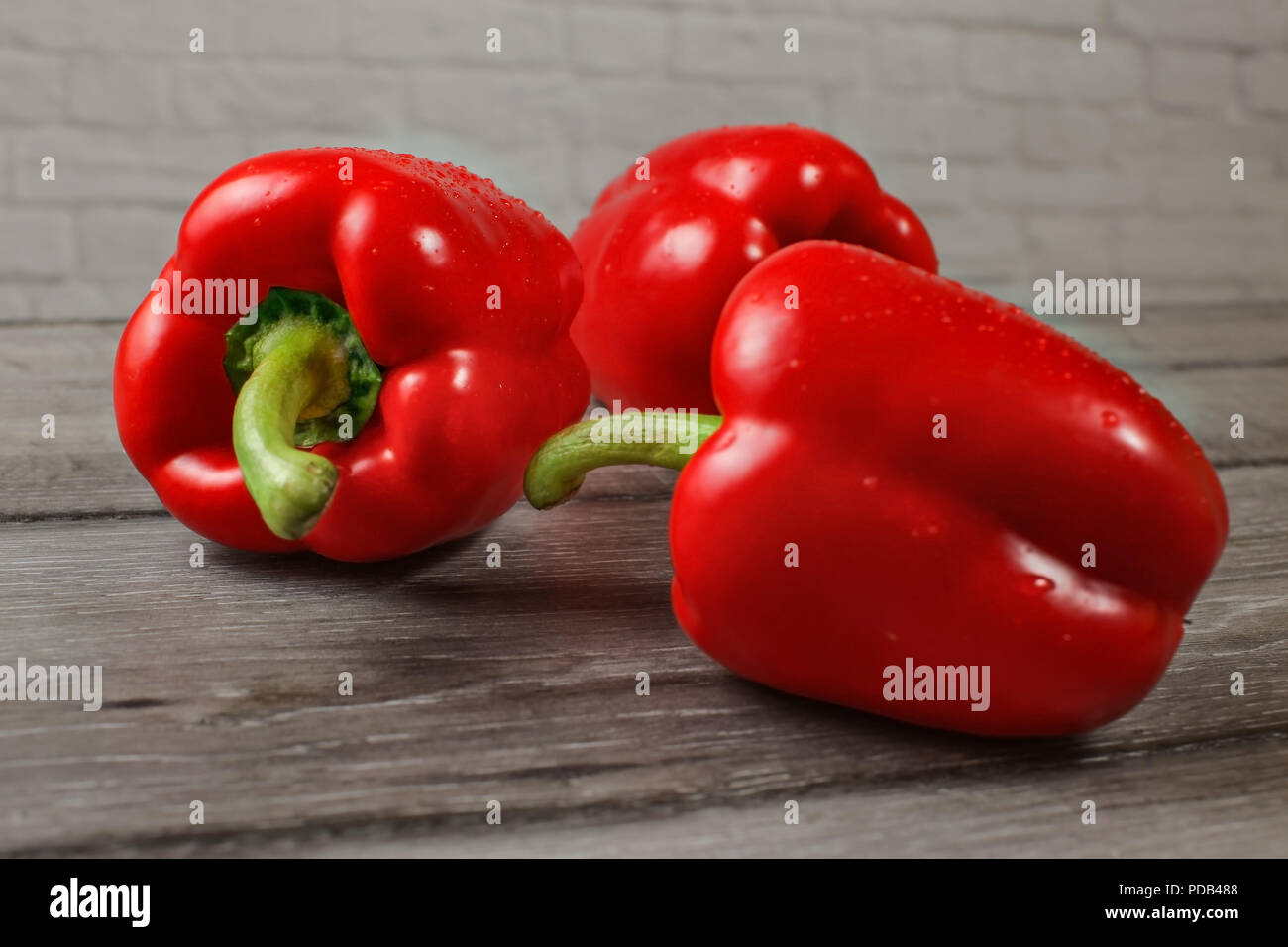 Drei helle rote Paprika auf hölzernen Schreibtisch, Fokus auf abfällt, Wasser. Stockfoto