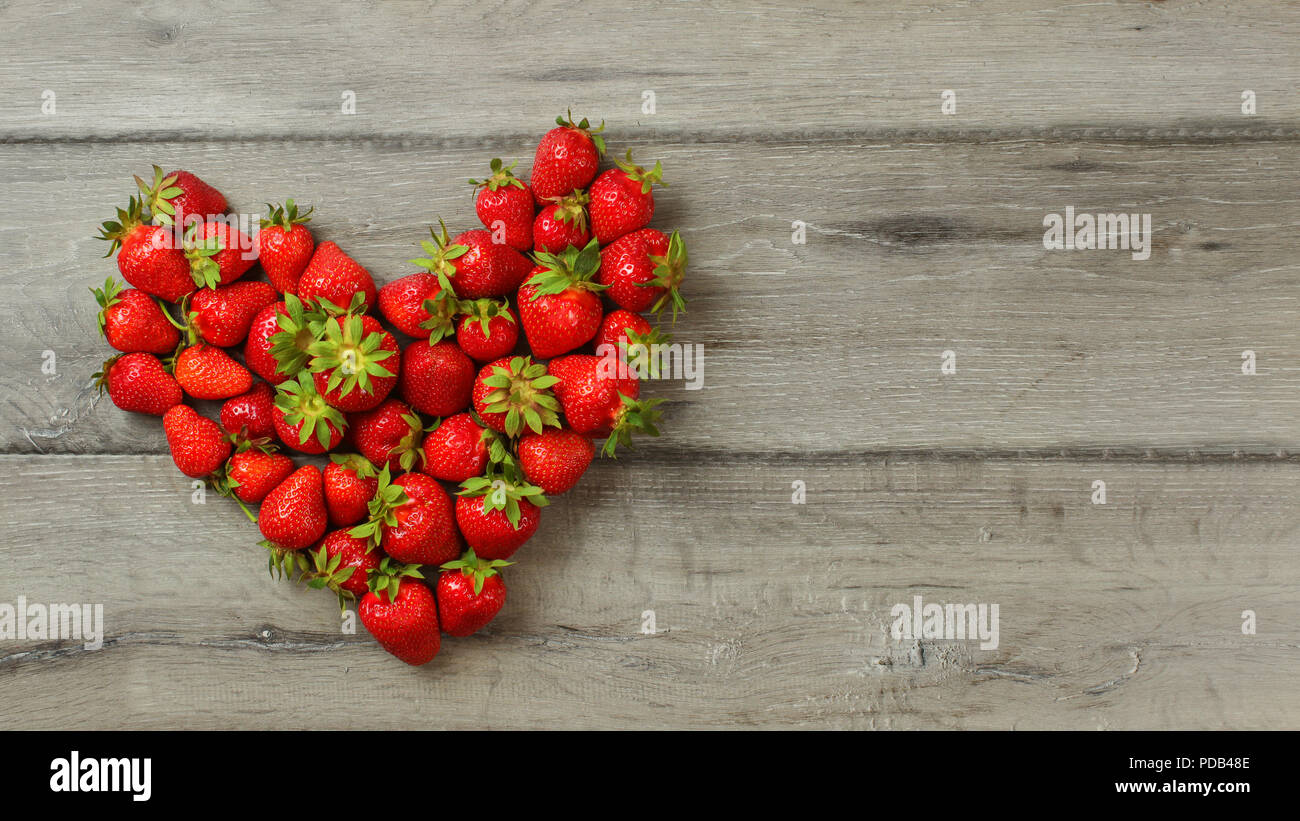 Tischplatte, Erdbeeren auf Holz Schreibtisch, in der Form des Herzens arrangiert, Platz für Text rechts. Stockfoto