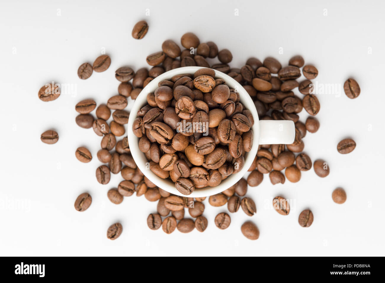 Weißes Porzellan Espresso Tasse gesehen von oben auf weißem Hintergrund mit braunen geröstete Kaffeebohnen überlaufen Stockfoto