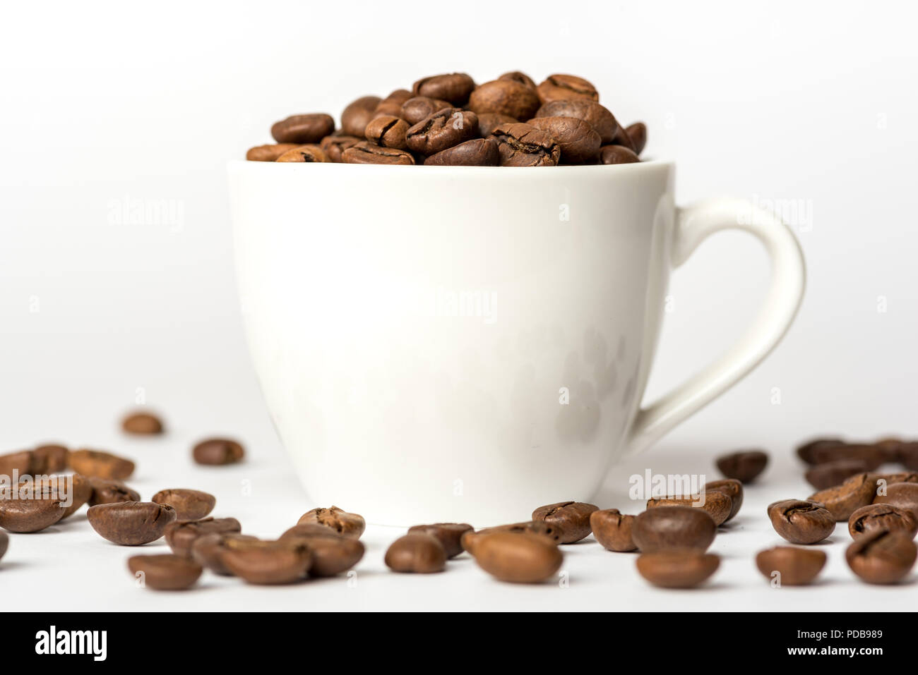 Weißes Porzellan Espresso Tasse auf weißem Hintergrund mit gerösteten Kaffeebohnen, die auf die Oberfläche ausgebreitet haben gefüllt Stockfoto