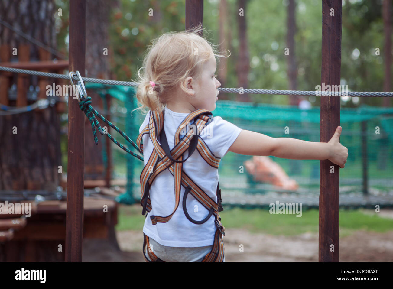 Kleine blonde Mädchen überwindet eine Barriere in einem Kabel Park. Stockfoto