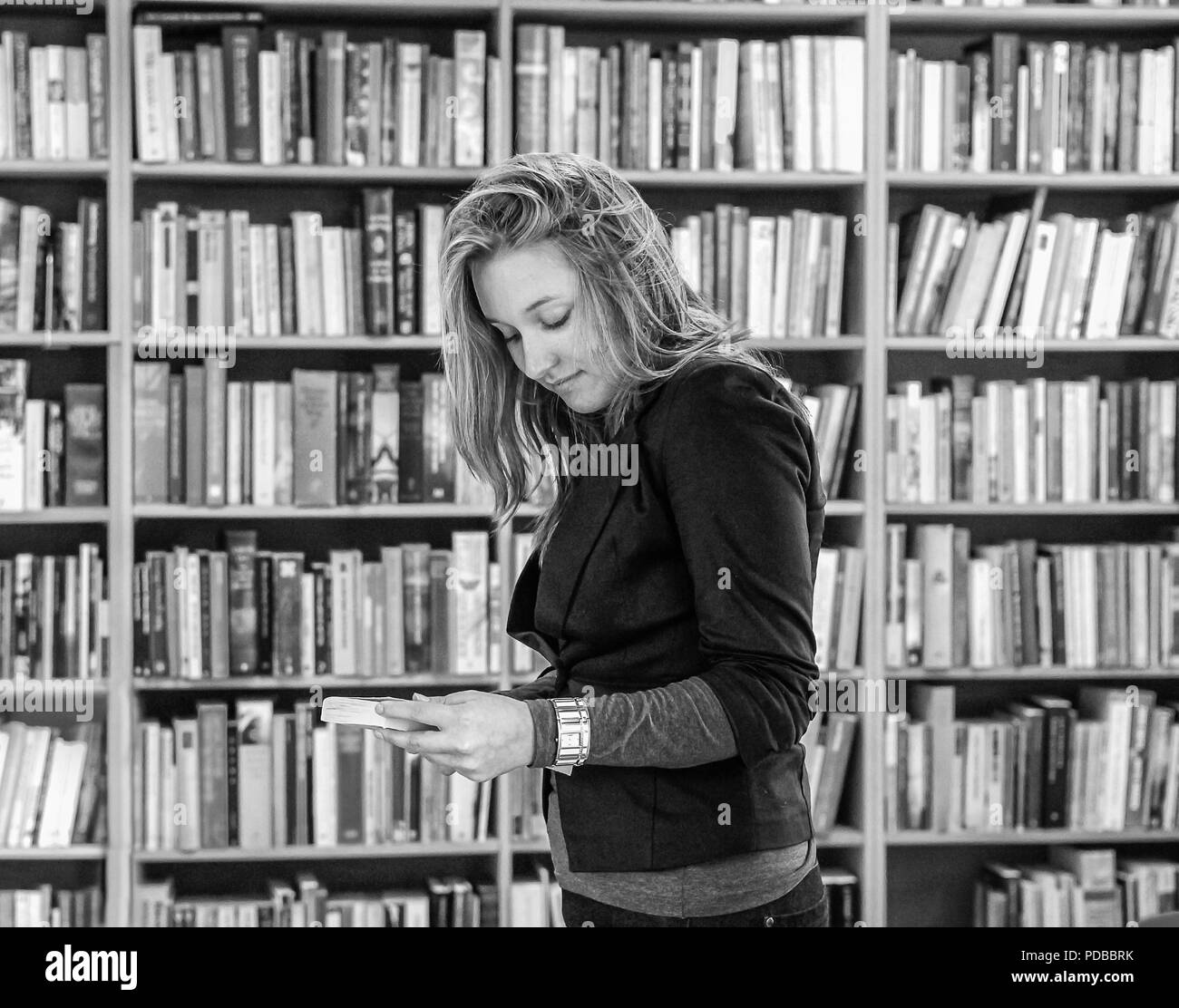 Junge Frau mit einem Buch vor der gestapelten Bücherregale in Schwarz und Weiß Stockfoto
