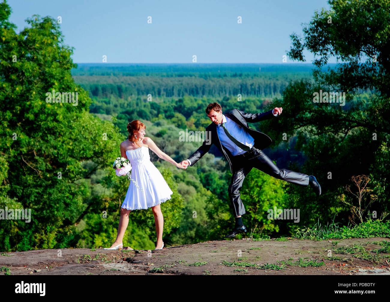 08.08.2018 Russland, Gebiet Brjansk. Braut und Bräutigam mit einem Blumenstrauß im Freien. Der Bräutigam Sprünge und hängt in der Luft. Stockfoto