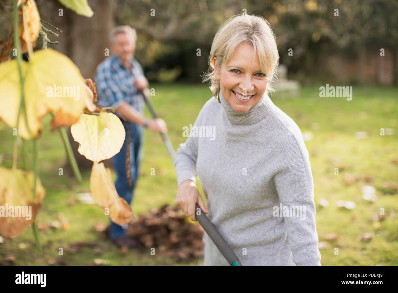 Porträt Lächeln, zuversichtlich, reife Frau harken Blätter im Herbst Hinterhof Stockfoto