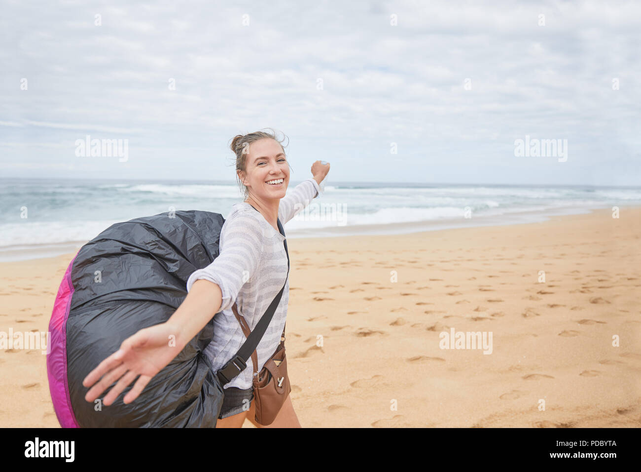 Porträt Lächeln, unbeschwerte Junge weibliche Gleitschirm mit Fallschirm Rucksack am Ocean Beach Stockfoto