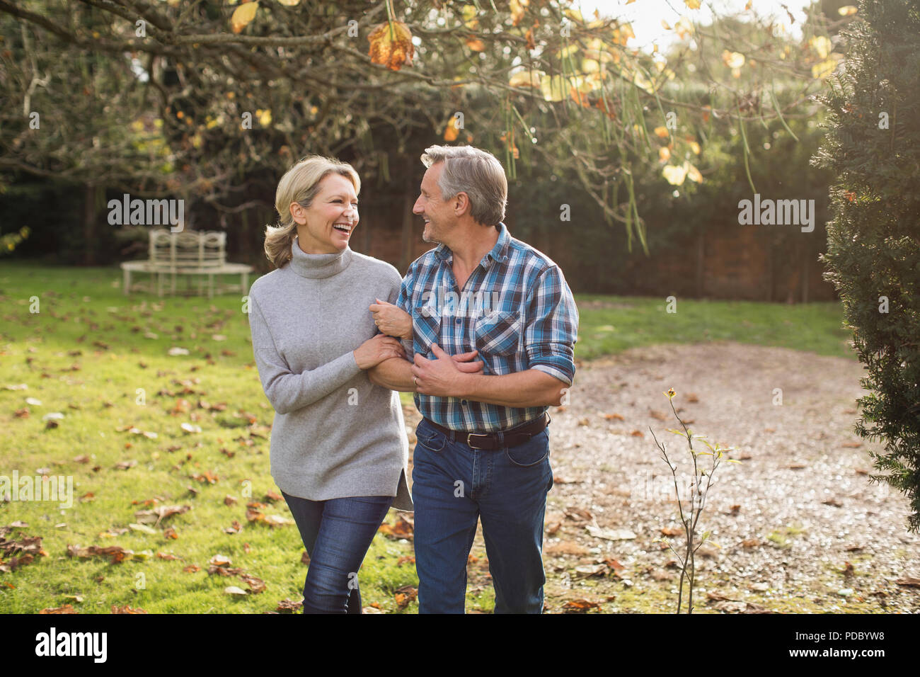 Glückliche, unbeschwerte Reifes Paar gehen Arm in Arm im sonnigen Herbst Hinterhof Stockfoto